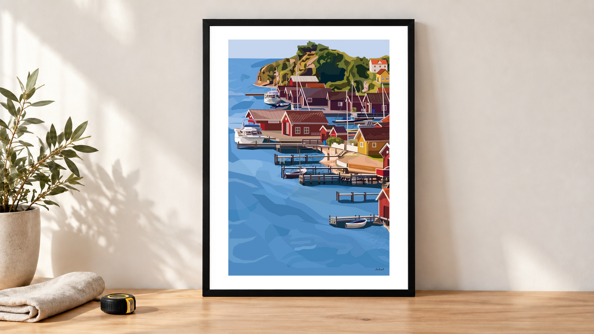 Illustration med Arksels Skärgården Poster i svart träram på ett ljust arbetsbord, med mjuk duk och måttband bredvid.